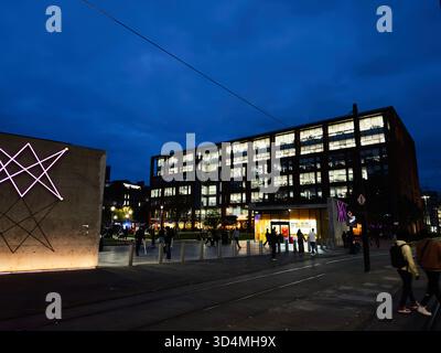 Manchester, Großbritannien - 30. September 2025: Eine lebhafte Manchester Street bei Nacht mit beleuchteten Büros, Kunstinstallationen und geschäftigen Fußgängern. Stockfoto