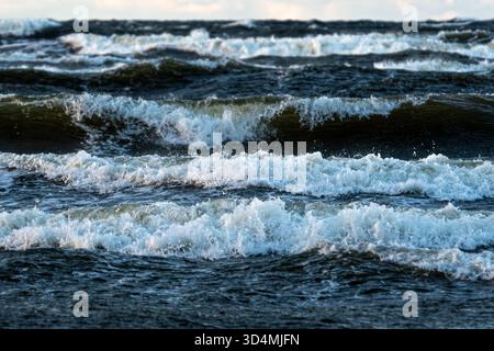Wellen Rollen und krachen gegen die Küste unter einem bewölkten Himmel im Nachmittagslicht. Stockfoto