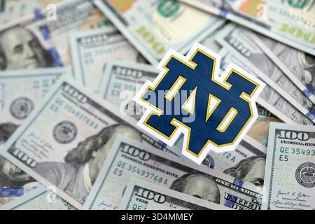 KIEW, UKRAINE - 23. FEBRUAR 2025 Notre Dame Fighting Irish Basketball Team Badge liegt auf einer großen Menge von hundert US-Dollar-Scheine Stockfoto