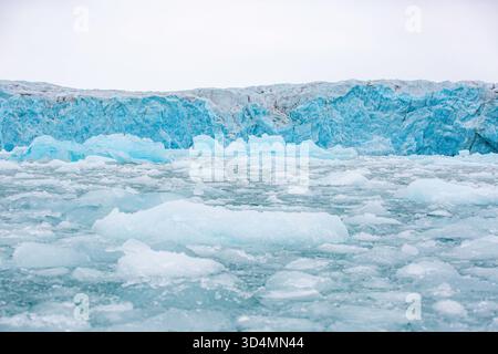 Svalbard Bootstour - großer Eiskörper mit einer blauen Wand im Hintergrund. Das Eis ist verstreut und zerbrochen, wobei einige Stücke im Wasser schwimmen. Th Stockfoto