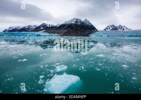 Svalbard Bootstour - großes Gewässer mit ein paar Eisbrocken, die darauf schwimmen. Das Wasser ist meist blau mit etwas weißem Eis Stockfoto
