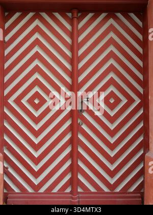 Historische Doppelflügeltür aus Holz mit rot-weißem Rautenmuster und altem Griff. Kopierraum Stockfoto