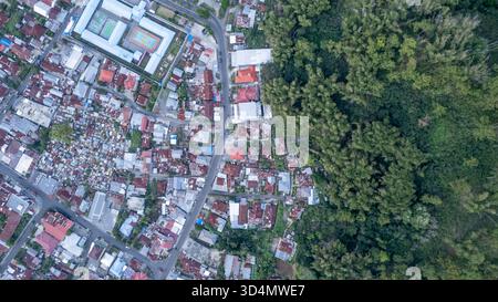 Ein Foto der Drohne von oben nach unten, das die Grenze der Stadt Bajawa in Indonesien zeigt. Dichte städtische Häuser mit rostigen Zinndächern treffen auf einen üppig grünen Wald. Stockfoto