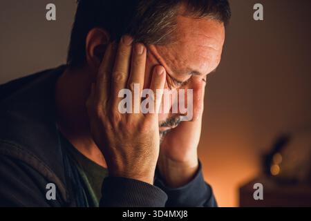 Leises Porträt eines Reifen Mannes in Verzweiflung, beleuchtet durch sanftes warmes Licht, symbolisiert Hoffnungslosigkeit und inneren Konflikt. Selektiver Fokus. Stockfoto