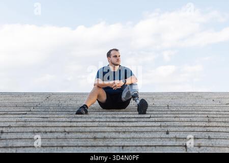 Porträt eines jungen, selbstbewussten Mannes mit Behinderung, mit einer Beinprothese, im Freien sitzend, auf den Straßentreppen. Motivation und Erfolgskonzept. Stockfoto