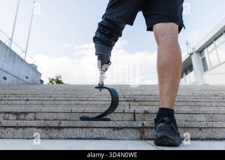 Mann in Sportbekleidung, der einen prothetischen Sportfuß trägt, der mit den Händen auf der Taille am Boden einer Außentreppe steht. Gewinnen, herausfordern und Ziel Stockfoto