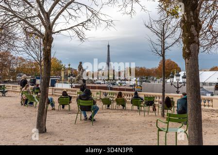 Paris, Frankreich, 11.10.2025. Menschen, die im Tuileriengarten auf grünen Gartenstühlen sitzen und an einem bewölkten Herbsttag auf den Eiffelturm blicken. Stockfoto