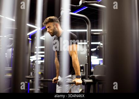 Ein junger Mann trainiert in einem stilvollen Fitnessstudio und baut mit Geräten Kraft auf. Die Atmosphäre ist energiegeladen und dynamisch und ergänzt sein Engagement. Stockfoto