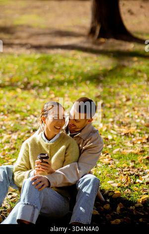 Koreanische Frau und kaukasischer Mann. Eine Koreanerin und ein kaukasischer Mann genießen einen gemütlichen Nachmittag im Park, umgeben von bunten Herbstblättern, lächelnd und lächelnd Stockfoto