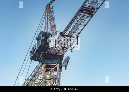 Die Nahaufnahme eines Turmdrehkrans erfasst den Stahlrahmen, die Kabel und die Fahrerkabine vor einem klaren Himmel. Fotografiert aus einem niedrigen vorderen Winkel, das Bild Stockfoto
