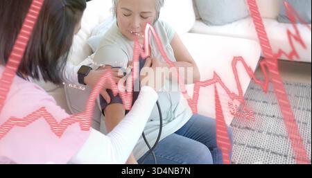 Seniorin in grünem Oberteil mit Blutdruckmanschette zu Hause, mit EKG-Überlagerung Stockfoto
