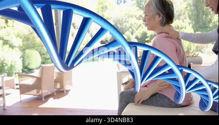 Sitzende asiatische Frau mit rosa Oberteil, die Hilfe auf der sonnigen Terrasse erhält, DNA Helix, Kopierraum Stockfoto