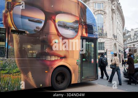 Fußgänger laufen hinter einem Schreibwarenbus mit einer großen Anzeige für einen Urlaub in Zypern an der Seite eines Londoner Busses in der Regent Street, am 11. November 2025 in London, England. Stockfoto