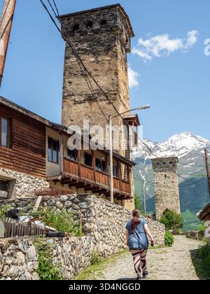 Mestia, Georgien - 9. Juni 2025: Touristen gehen zu den alten svan Türmen auf der Straße in Mestia Stadt in Samegrelo-Zemo Svaneti Provinz Georgien auf sonnigem su Stockfoto