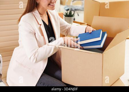 Beweglicher Tag. Frau, die im Büro Bücher in Pappkarton legt, Nahaufnahme Stockfoto