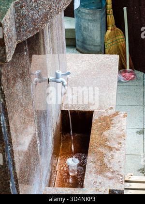 Heißes natürliches Mineralwasser wird im Central Park in Borjomi Resort Town, Georgia, am Sommertag aus dem Frühling in Glas gegossen Stockfoto