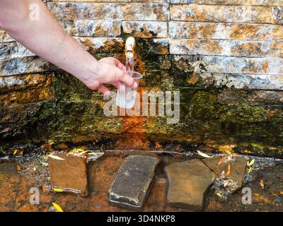 Man gießt natürliches Mineralwasser aus der kalten Quelle in Glas in der Nähe des Central Parks in Borjomi Resort Town, Georgia am Sommertag Stockfoto