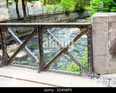 Alte Brücke, die am sonnigen Sommertag über den Borjomula River im Central Park in Borjomi Resort, Georgia, geländer Stockfoto
