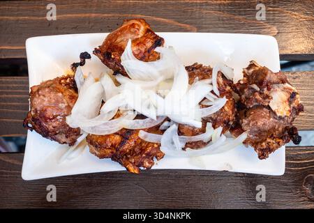 Blick von oben auf das georgianische Lamm-Schaschlik Mtsvadi auf weißem Teller auf Holztisch in einem lokalen Outdoor-Café in Borjomi Stadt, Georgia am Sommertag Stockfoto