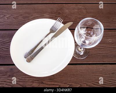 Tisch im Straßencafé - Blick von oben auf die weiße Tafel mit Messer und Gabel und leeren Glasweinkelch auf Holztisch im Straßencafé in Batumi City, Stockfoto