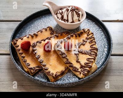 Pfannkuchen mit Schokoladenmuster, Erdbeeren und Eis in separater Schüssel auf Keramikplatte auf Holztisch Stockfoto
