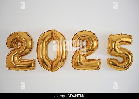 Einfache, minimalistische Grußkarte mit goldenen Ballons in Form 2025 an weißer Wand - Happy New Year and Merry Christmas Concept. Stockfoto