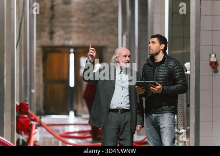 Zwei Männer diskutieren in einer zeitgenössischen Industriefabrik über die Ausrüstung und das Layout um sie herum. Stockfoto