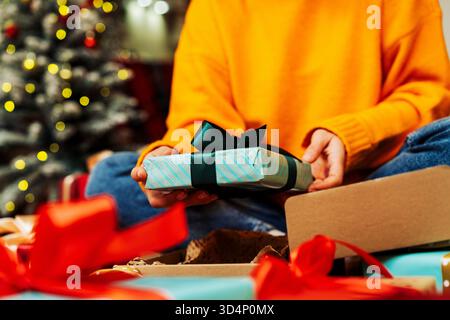 Frau mit gelbem Pullover, die zu Hause Weihnachtsgeschenke auf dem Boden auspackt. Stockfoto