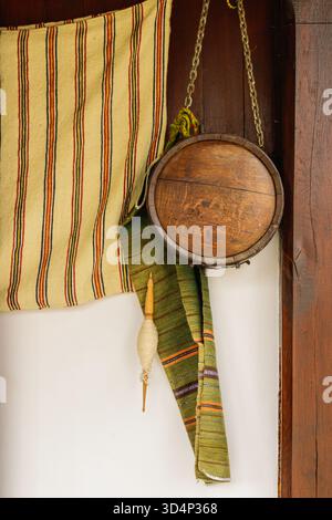 Eine Komposition aus einer handgefertigten hölzernen Kantine und bunten gewebten Textilien, die an einer Holzwand hängen. Die warmen Töne und traditionellen Texturen erinnern an rura Stockfoto