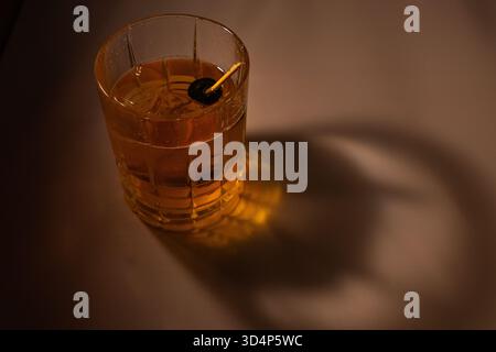 Ein raffinierter Cocktail auf Whiskey-Basis, serviert in einem klaren Glas mit großem Eiswürfel und Kirschgarnitur, Stockfoto