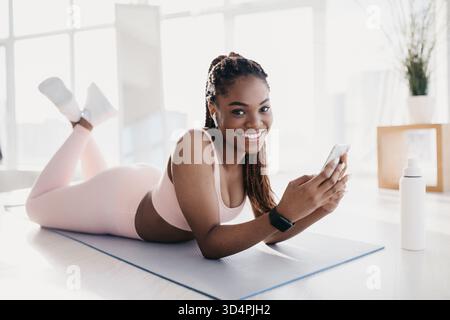 Black Woman genießt die Trainingspause, während sie Musik hört und ihr Smartphone zu Hause nutzt Stockfoto