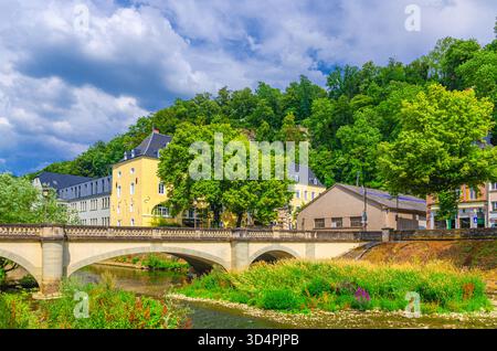 Landschaft mit grünen Bäumen und Büschen am Ufer und Brücke über den Fluss Alzette, alten Gebäuden und Park auf einem Hügel im Viertel Grund des Luxemburger Stadthistors Stockfoto