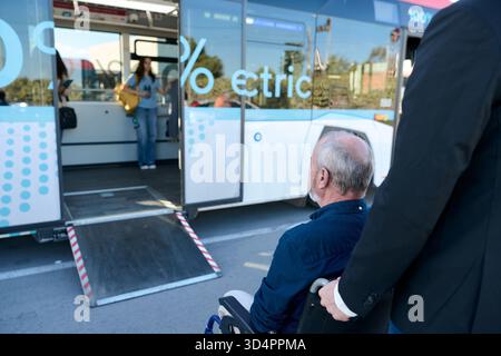 Assistentin, die einem älteren Mann im Rollstuhl hilft, in einem Elektrobus zu steigen Stockfoto