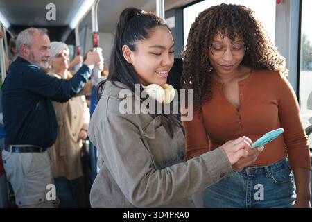 Verschiedene Freundinnen teilen sich ein Smartphone in öffentlichen Verkehrsmitteln Stockfoto