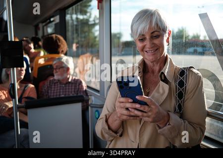 Eine ältere Frau lächelt, während sie im Bus pendelt Stockfoto
