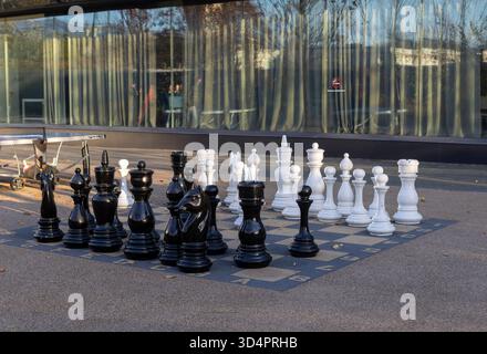 Große Schachfiguren stehen auf einem Schachbrett im Freien und laden die Spieler ein, ein strategisches Spiel unter freiem Himmel zu genießen. Stockfoto