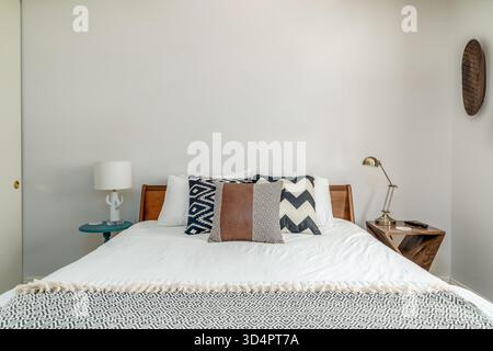Moderne Einrichtung im Wüstenzimmer. Holzrahmenbett, Akzentkissen, Lampen, Nachttische. Vorderansicht. Stockfoto