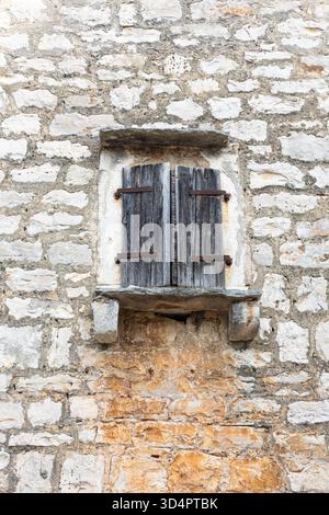 Ein verwittertes Paar Holzläden bedeckt eine alte Steinmauer mit rostigen Scharnieren und abgebrochener Farbe. Die alte Textur erinnert an ländlichen Charme, Geschichte, Stockfoto