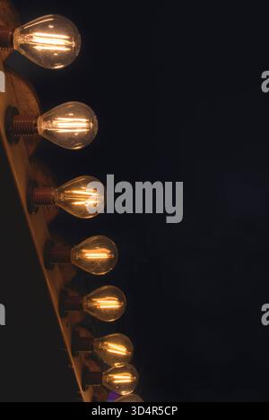 Eine Reihe von Glühbirnen wird beleuchtet, was eine warme und gemütliche Atmosphäre schafft. Die Glühlampen sind in einer geraden Linie angeordnet, wobei einige Glühlampen sich leicht überlappen Stockfoto