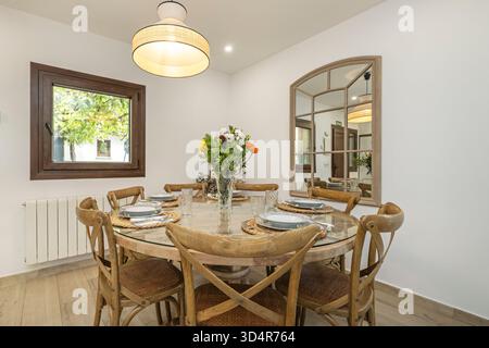 Speiseset mit rundem lackiertem Kieferntisch und Korbstühlen, mit einem Strauß von bunten Gerbera-Gänseblümchen Stockfoto