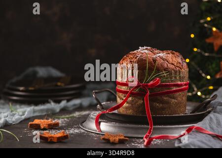 Ein traditioneller italienischer Panettone, der mit Puderzucker bestäubt und mit einem dekorativen roten Band umwickelt ist, wird auf einem Vintage-Serviertablett aus Metall präsentiert. Th Stockfoto
