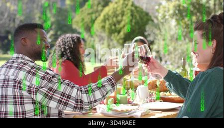 Gruppe mit anklirenden Weingläsern und lässigen Hemden, die sich einen Gartentisch teilen, mit Braten und Daten überlagert Stockfoto