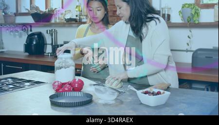 Zwei Frauen in Schürzen Formen, die Teig auf der Kücheninsel bearbeiten, mit Mehlbecher, Sieb Stockfoto
