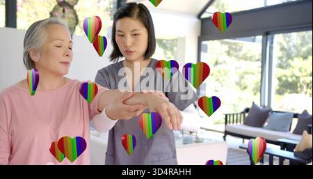Krankenschwester in grauen Peelings hilft Senioren in rosafarbenem Oberteil im Wohnzimmer und führt den Arm mit Regenbogenherzen Stockfoto