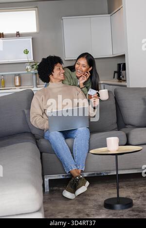 Stöbern Sie in verschiedenen Paaren mit Kreditkarte in der offenen Küche, mit Laptop und Kaffeetassen Stockfoto