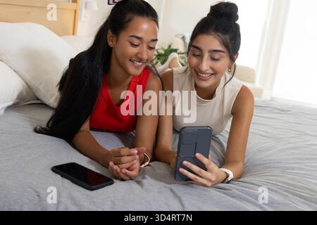 Liegend verschiedene weibliche Freunde mit Smartphone auf dem Bett im hellen Schlafzimmer, mit Ersatztelefon Stockfoto