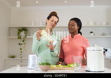 Verschiedene weibliche Freunde bereiten grünen Smoothie in der Küche zu, mit Mixer und frischem Gemüse Stockfoto