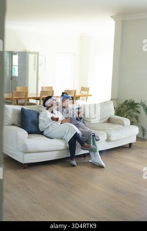 Verschiedene Freundinnen schlürfen Kaffee aus roten Tassen auf dem Sofa im Wohnzimmer und zeigen einen ruhigen Morgen Stockfoto