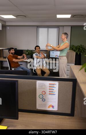 Dehnen Sie verschiedene Kollegen, die an Schreibtischen im Großraumbüro trainieren, mit ergonomischen Stühlen und Monitoren Stockfoto
