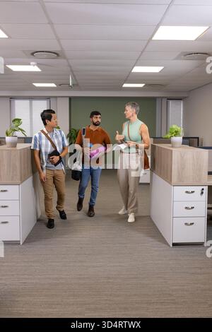 Verschiedene Kollegen mit Smartphone und Notebook im Bürokorridor mit Topfpflanzen laufen Stockfoto